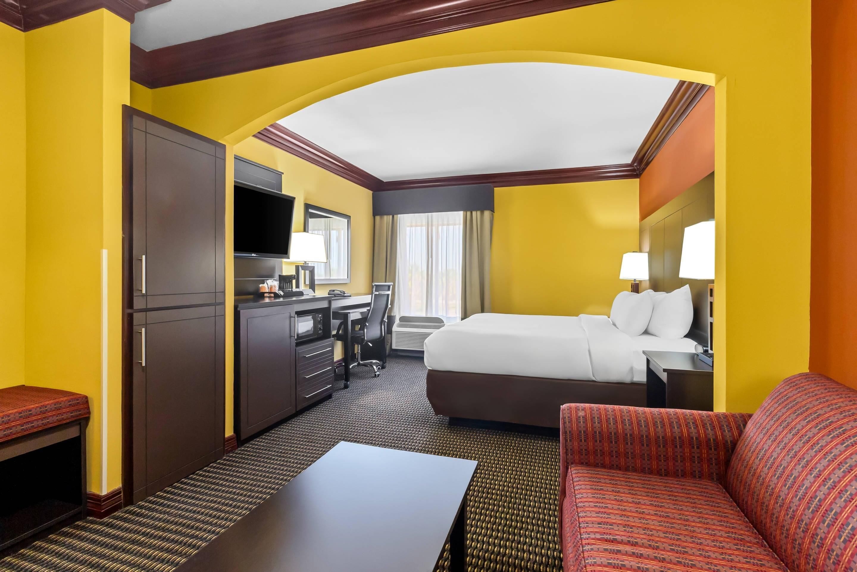 A hotel room with a bed, desk, chair, and a sofa.