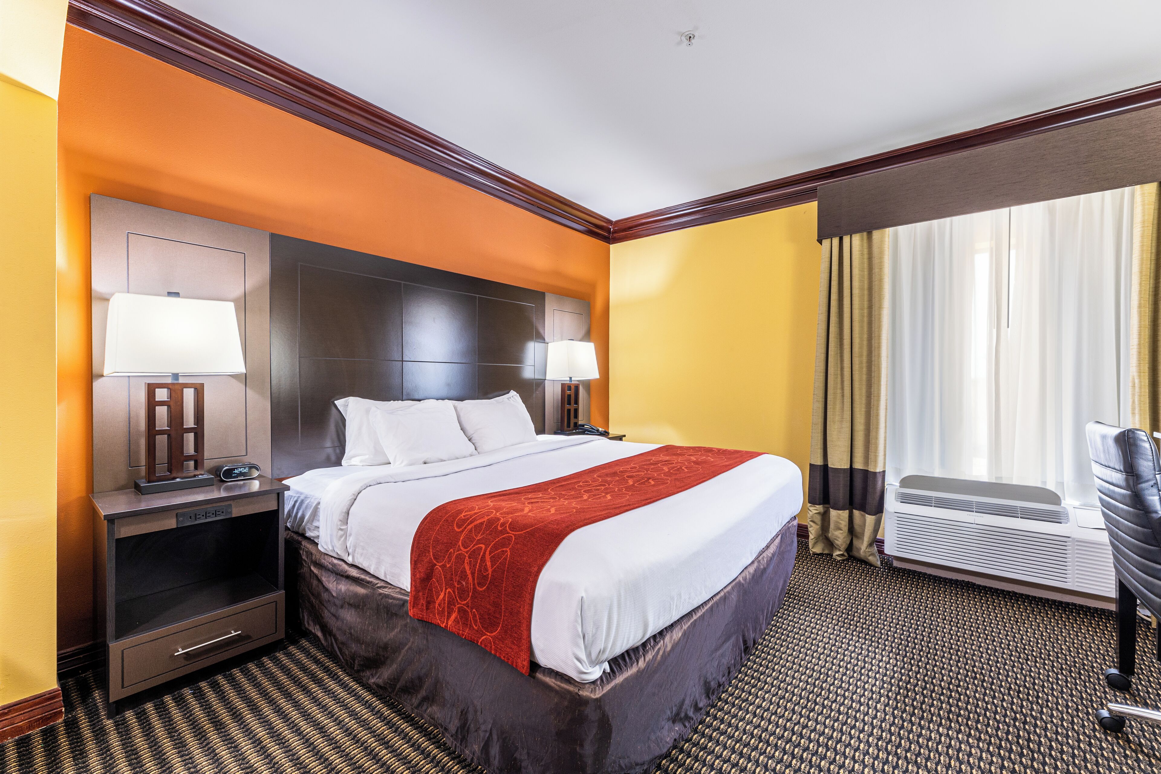 A hotel room with a large bed, two bedside tables with lamps, a chair, and a window with curtains.