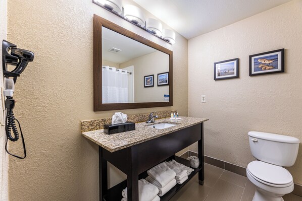 A bathroom with a granite countertop sink, a mirror, a toilet, and two framed pictures on the wall. - Comfort Suites Lake Jackson Clute (Lake Jackson)