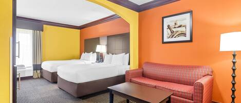 Una habitación de hotel con dos camas, un sofá, una mesita y una lámpara.