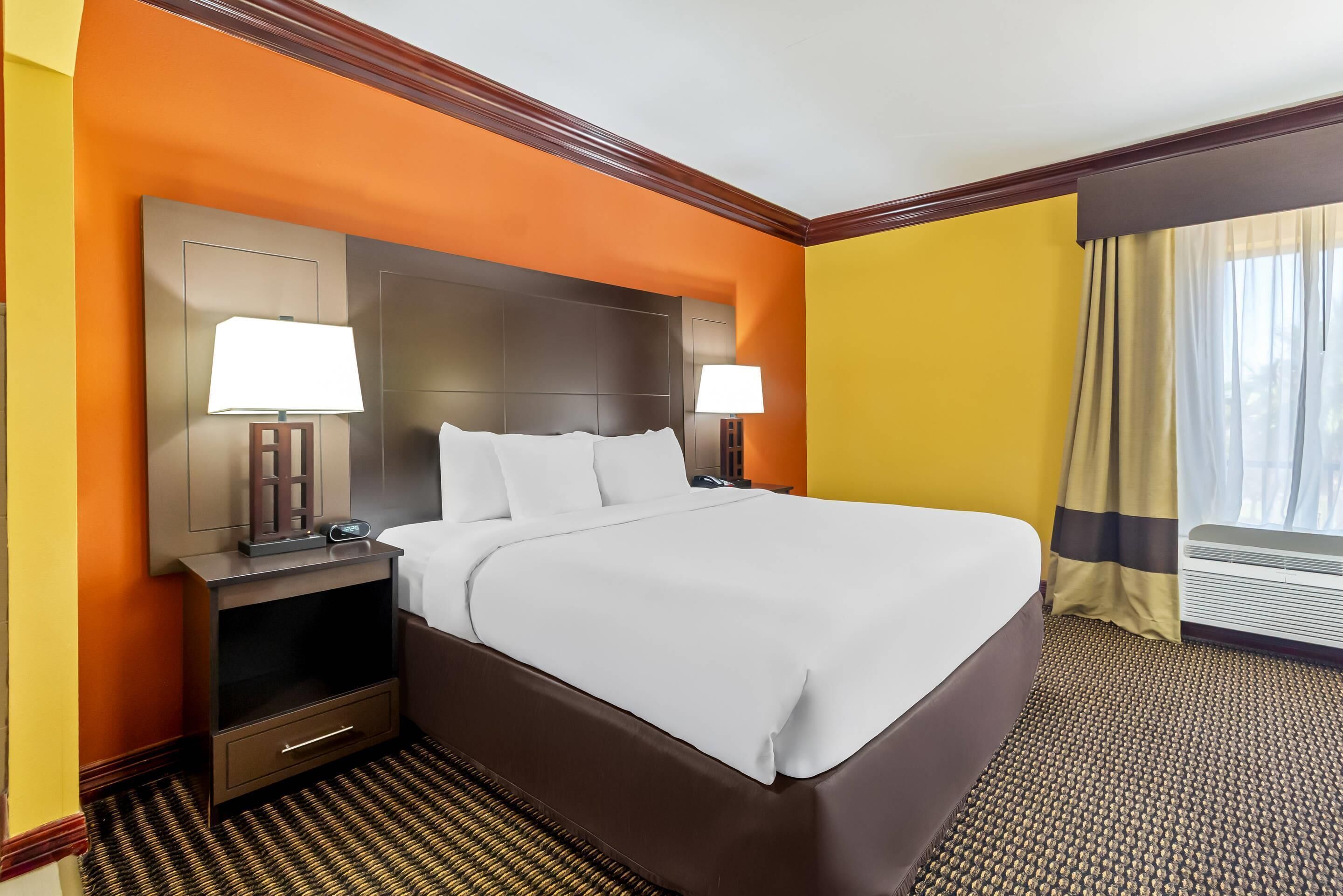Habitación de hotel con una cama grande, dos mesitas de noche con lámparas, un televisor de pantalla plana y una ventana con cortinas.