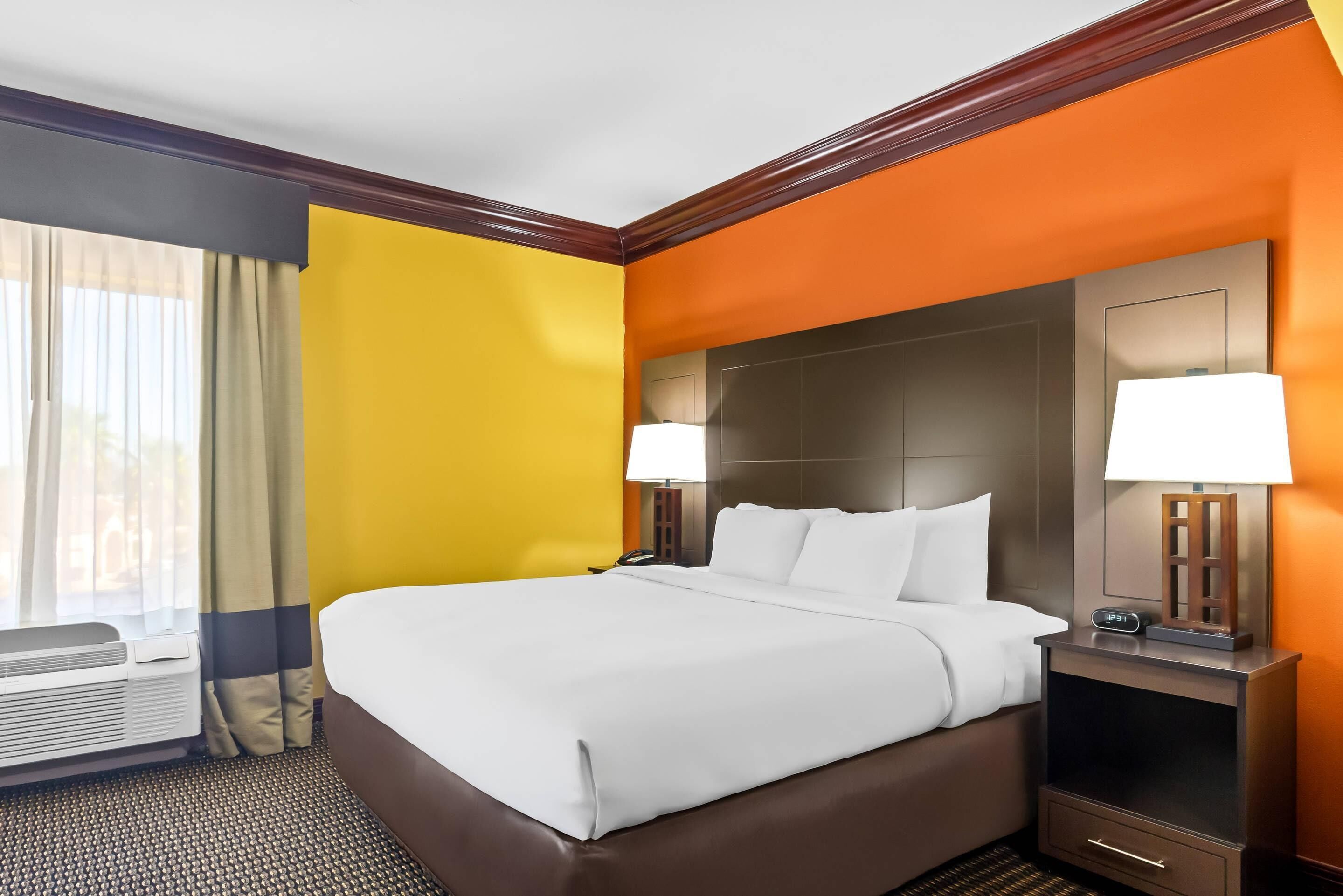A hotel room with a large bed, two bedside lamps, a nightstand, and a window with curtains.