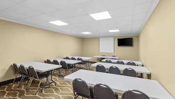 A conference room with multiple tables and chairs, a projector screen, and a carpeted floor.