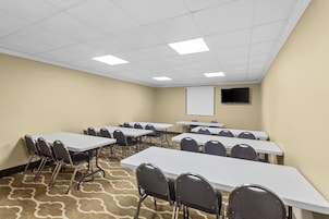 Una sala de conferencias con varias mesas y sillas, una pantalla de proyector y piso alfombrado.