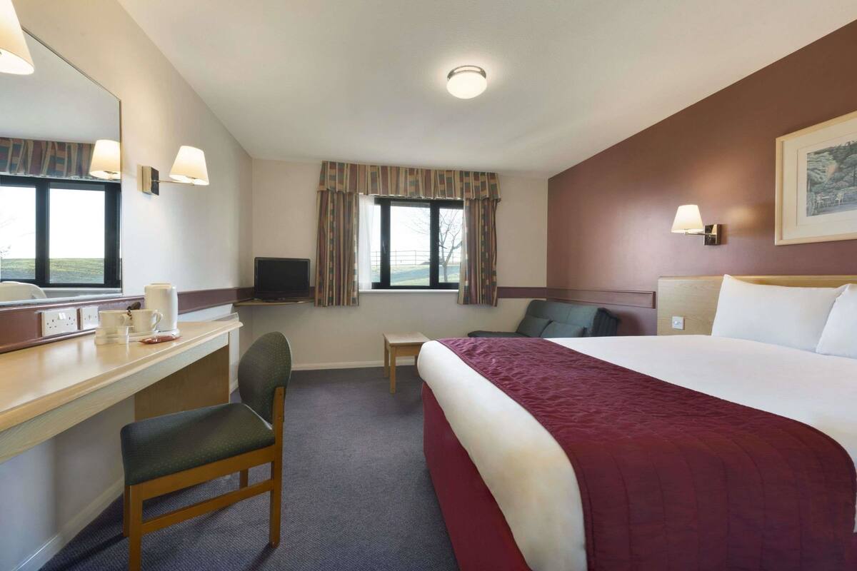 A hotel room with a bed, a desk with a chair, a television, and a window with curtains.