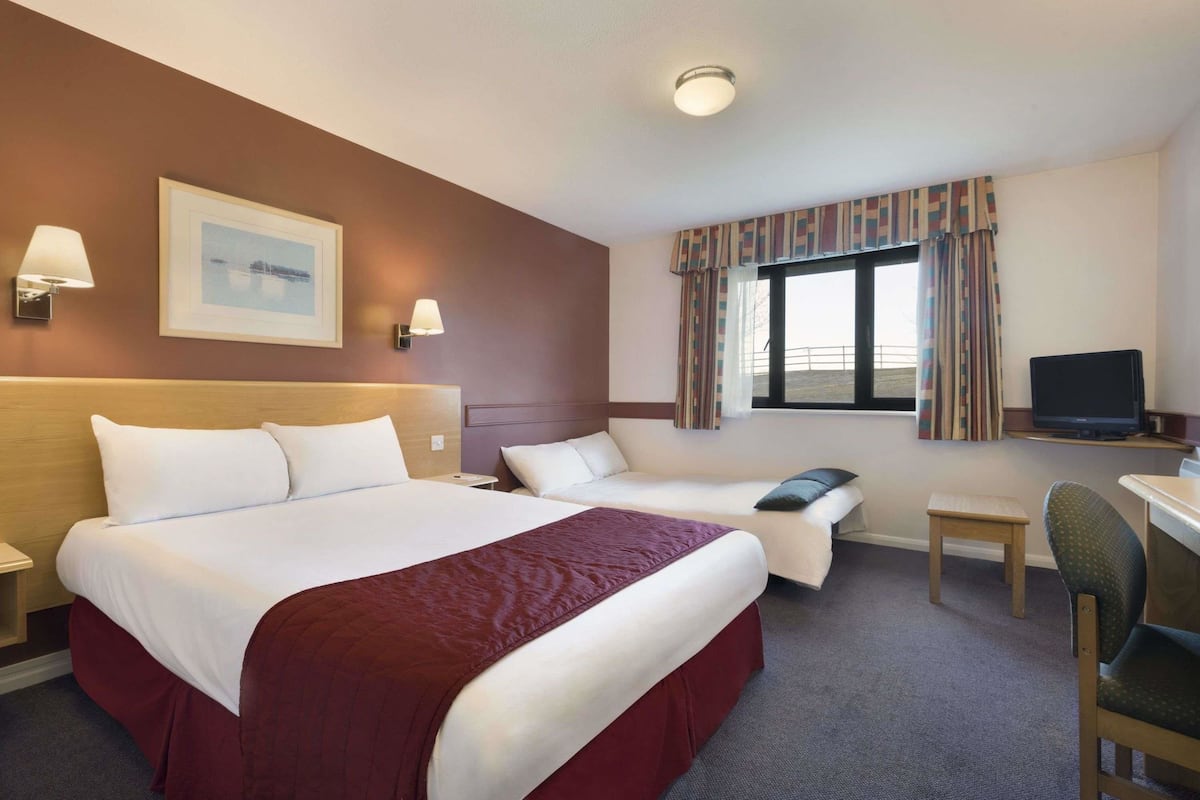 A hotel room with a large bed, a smaller bed, a desk, a chair, a television, and a window with curtains.