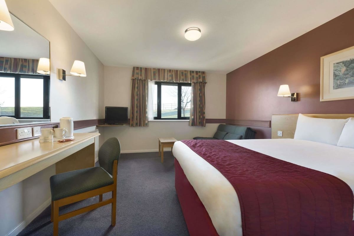 A hotel room with a bed, desk, chair, television, and a window with curtains.
