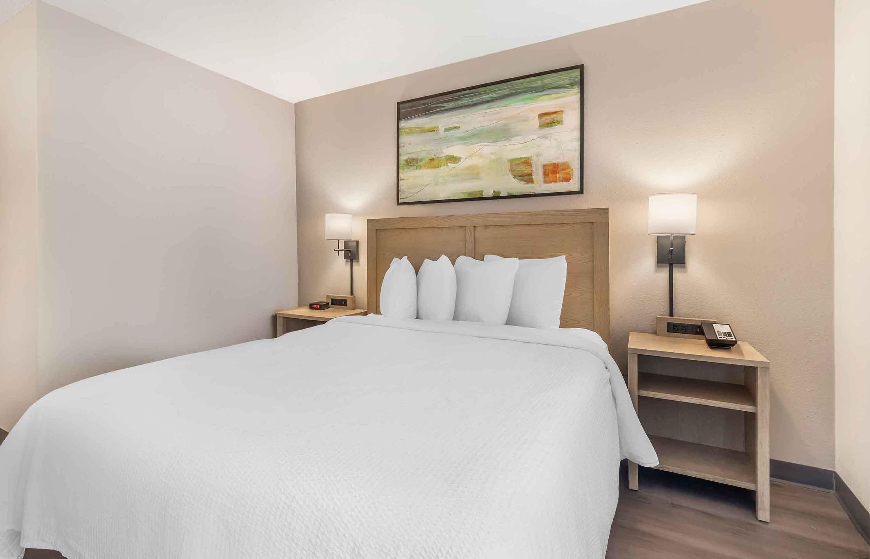 Habitación de hotel con una cama grande, dos mesitas de noche con lámparas, un cuadro en la pared y un cabecero de madera.