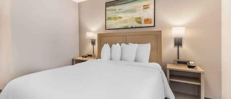 Habitación de hotel con una cama grande, dos mesitas de noche con lámparas, un cuadro en la pared y un cabecero de madera.