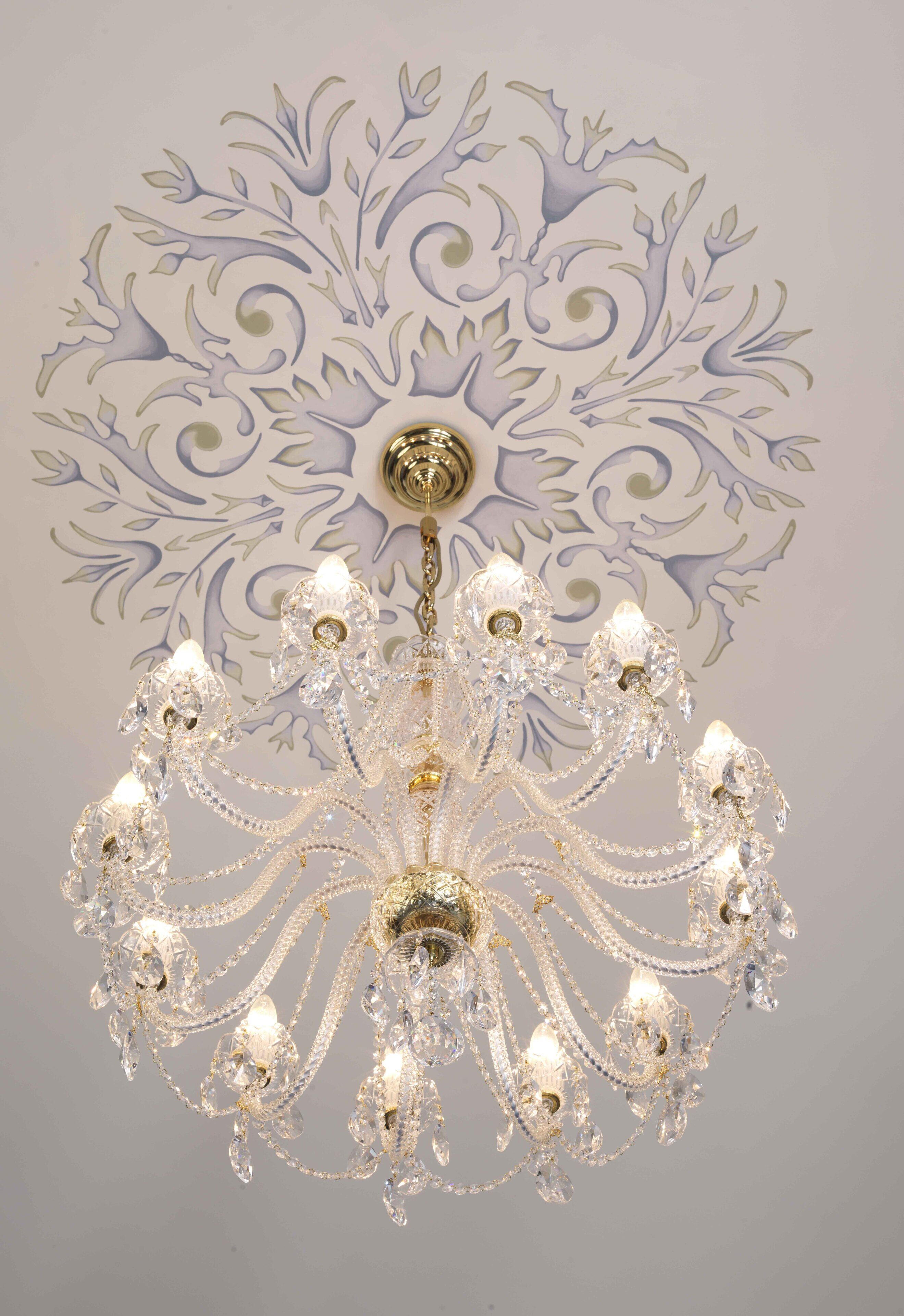 A chandelier with multiple crystal arms and lights, set against a wall with a decorative pattern.