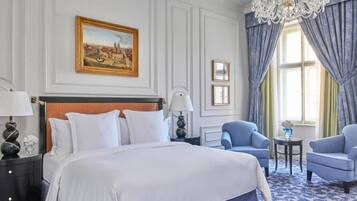 A hotel room with a large bed, two armchairs, a chandelier, and a painting on the wall.