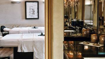Een hotelkamer met een bed, nachtkastje en een grote spiegel die een kroonluchter weerspiegelt.