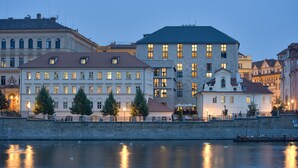 A waterfront hotel with multiple floors, a stone facade, and a reflection in the water. - Four Seasons Hotel Prague (Prague)