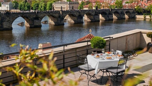 A terrace with a table set for dining, overlooking a river and a bridge. - Four Seasons Hotel Prague (Prague)
