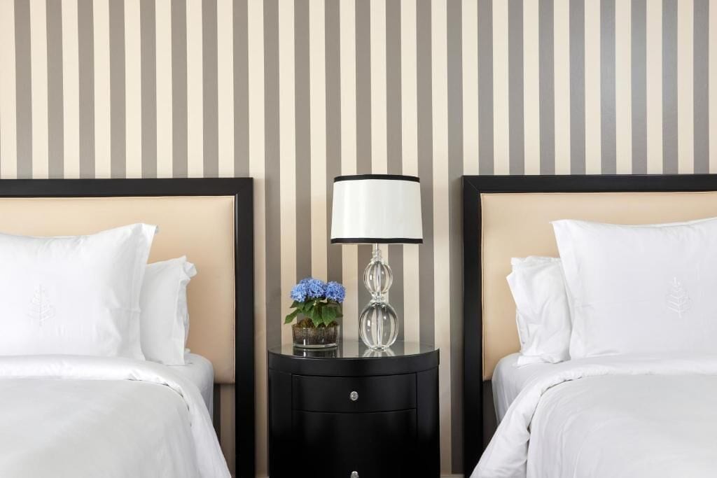 Ein Hotelzimmer mit zwei Betten, einem Nachttisch mit Lampe und einer gestreiften Wand.
