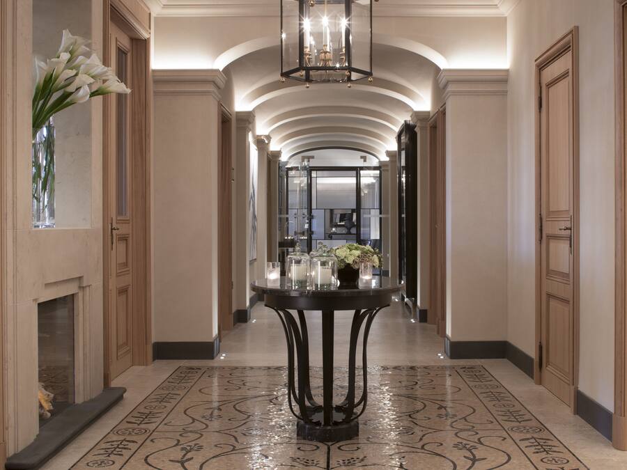 A hallway with a round table in the center, flanked by wooden doors and a fireplace.
