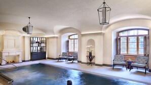 An indoor swimming pool with a person in the water, surrounded by seating and a fireplace. - Four Seasons Hotel Prague (Prague)