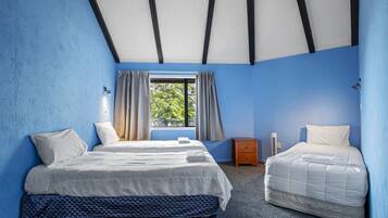 A room with two beds, a window with curtains, a small bedside table, and a radiator.