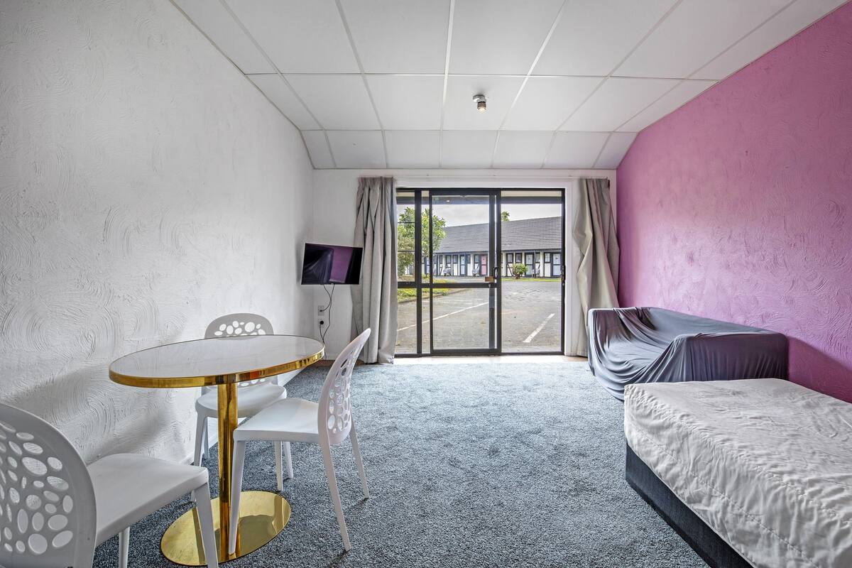 A hotel room with a bed, a round table with chairs, a TV, and a view of the outside.