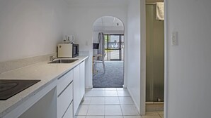 A narrow hallway leading to a balcony with a view, a kitchen area with white cabinets and a countertop, and a door with a towel hanging on it. - Oakwood Manor Motor Lodge (Auckland)