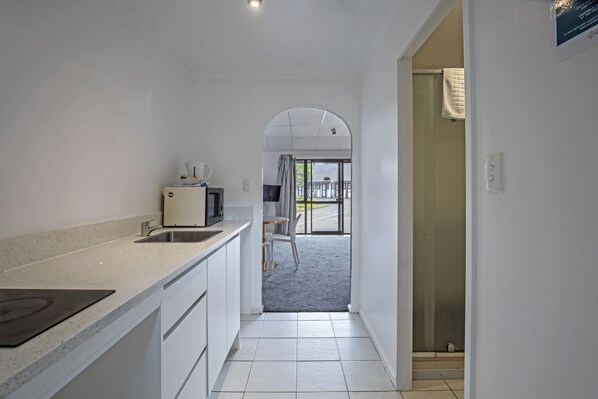 A narrow hallway leading to a balcony with a view, a kitchen area with white cabinets and a countertop, and a door with a towel hanging on it. - Oakwood Manor Motor Lodge (Auckland)