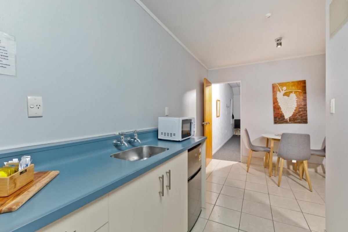 A modern kitchen with a blue countertop, stainless steel sink, and a microwave. There is a dining area with a table and chairs.