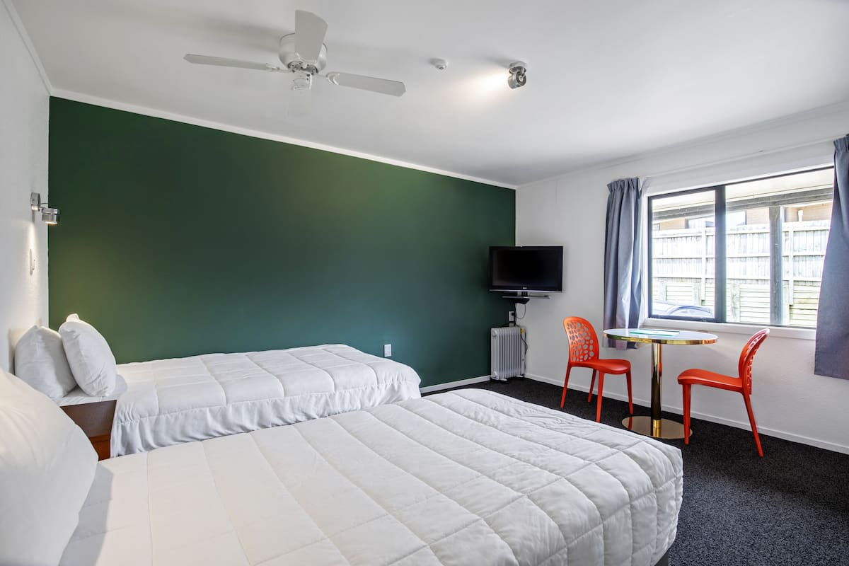 A hotel room with two beds, a TV, a table with two chairs, and a window with curtains.