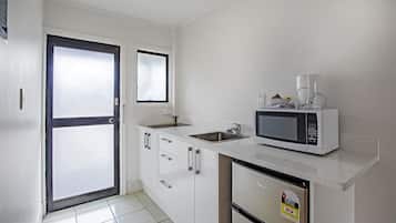 A compact kitchen with white cabinets, a stainless steel refrigerator, a microwave, and a sink.