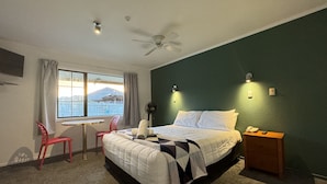 A hotel room with a bed, a desk, a chair, a ceiling fan, and a window with curtains. - Oakwood Manor Motor Lodge (Auckland)