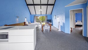 A modern kitchen with a built-in microwave, a dining area with a table and chairs, and a bedroom with a bed and a window. - Oakwood Manor Motor Lodge (Auckland)