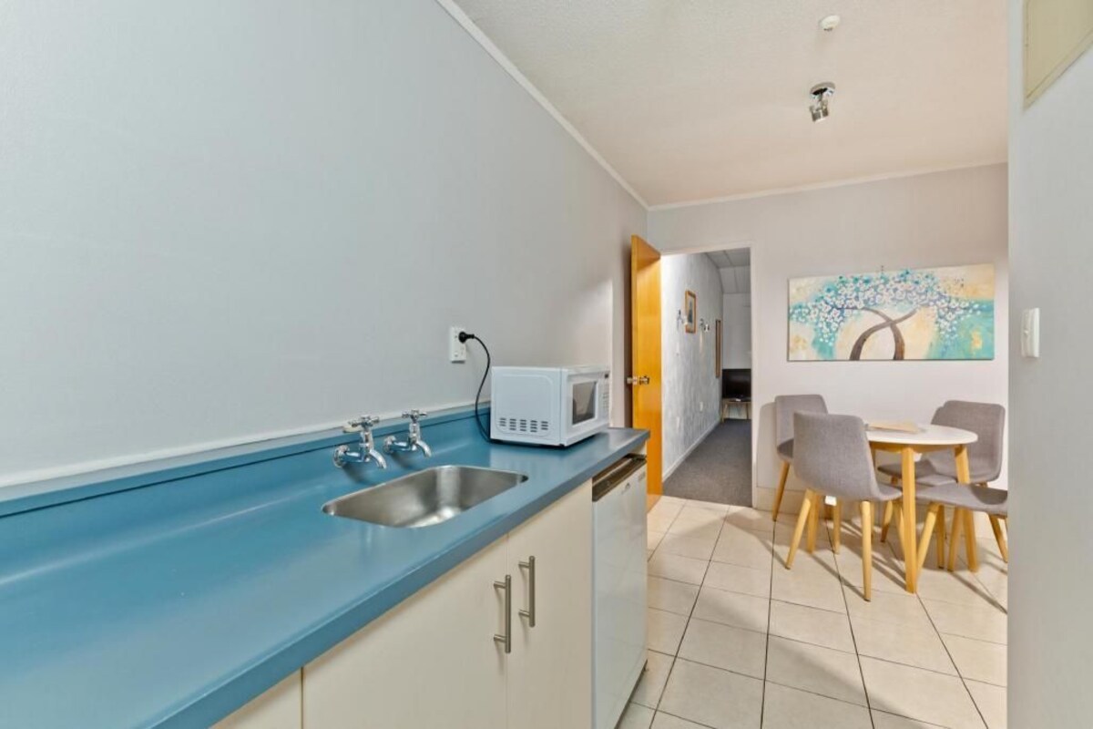 A compact kitchen with a blue countertop, a microwave, and a sink. There is a dining area with a table and chairs.