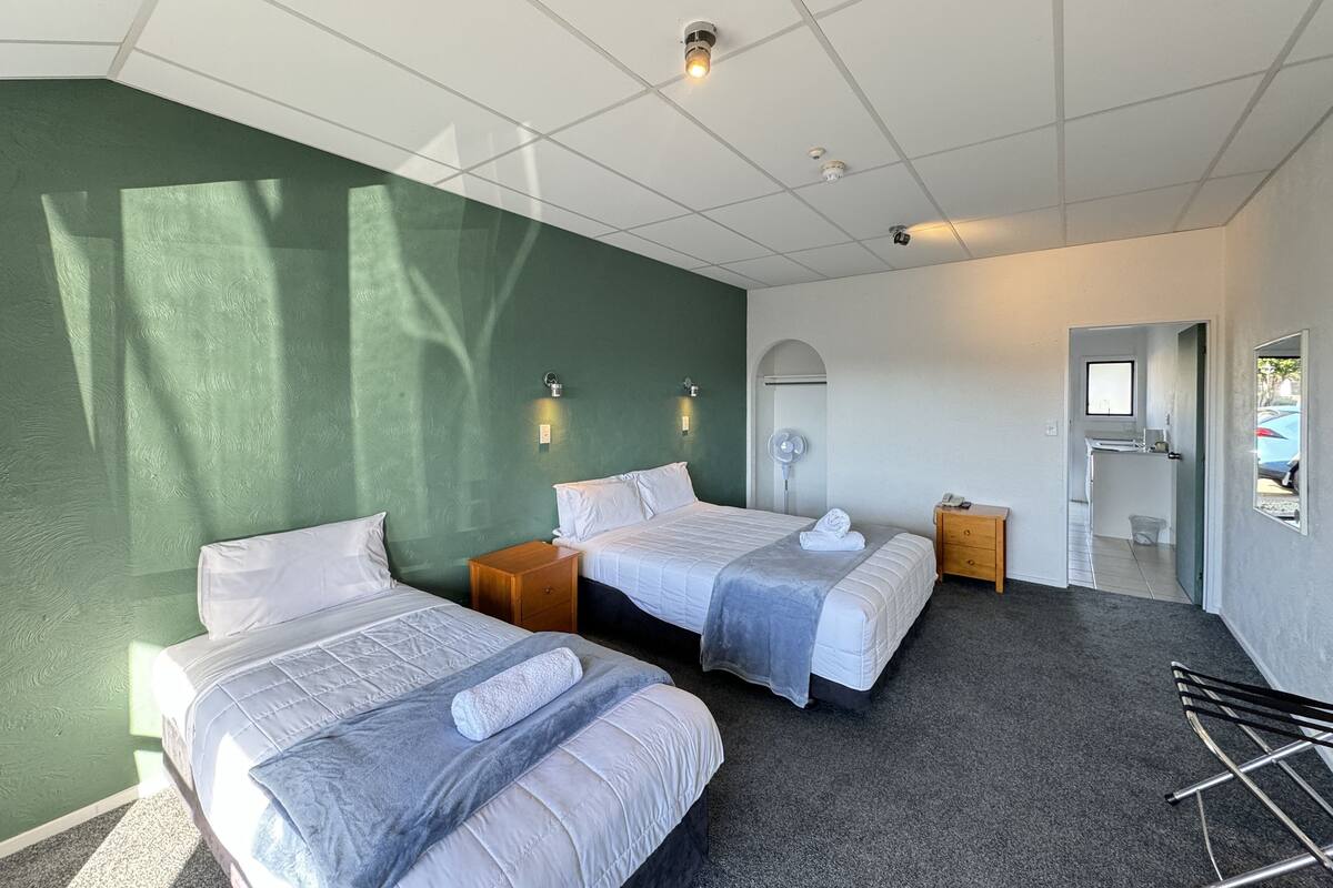 A hotel room with two beds, a small wooden side table, a desk with a chair, a mirror, and a view of the outside.