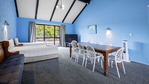 A room with a large window, a bed, a dining table with chairs, and a TV. - Oakwood Manor Motor Lodge (Auckland)
