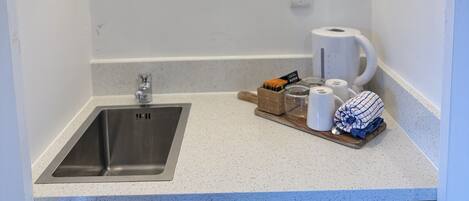 A compact kitchen with a stainless steel sink, a coffee maker, and a dish rack.