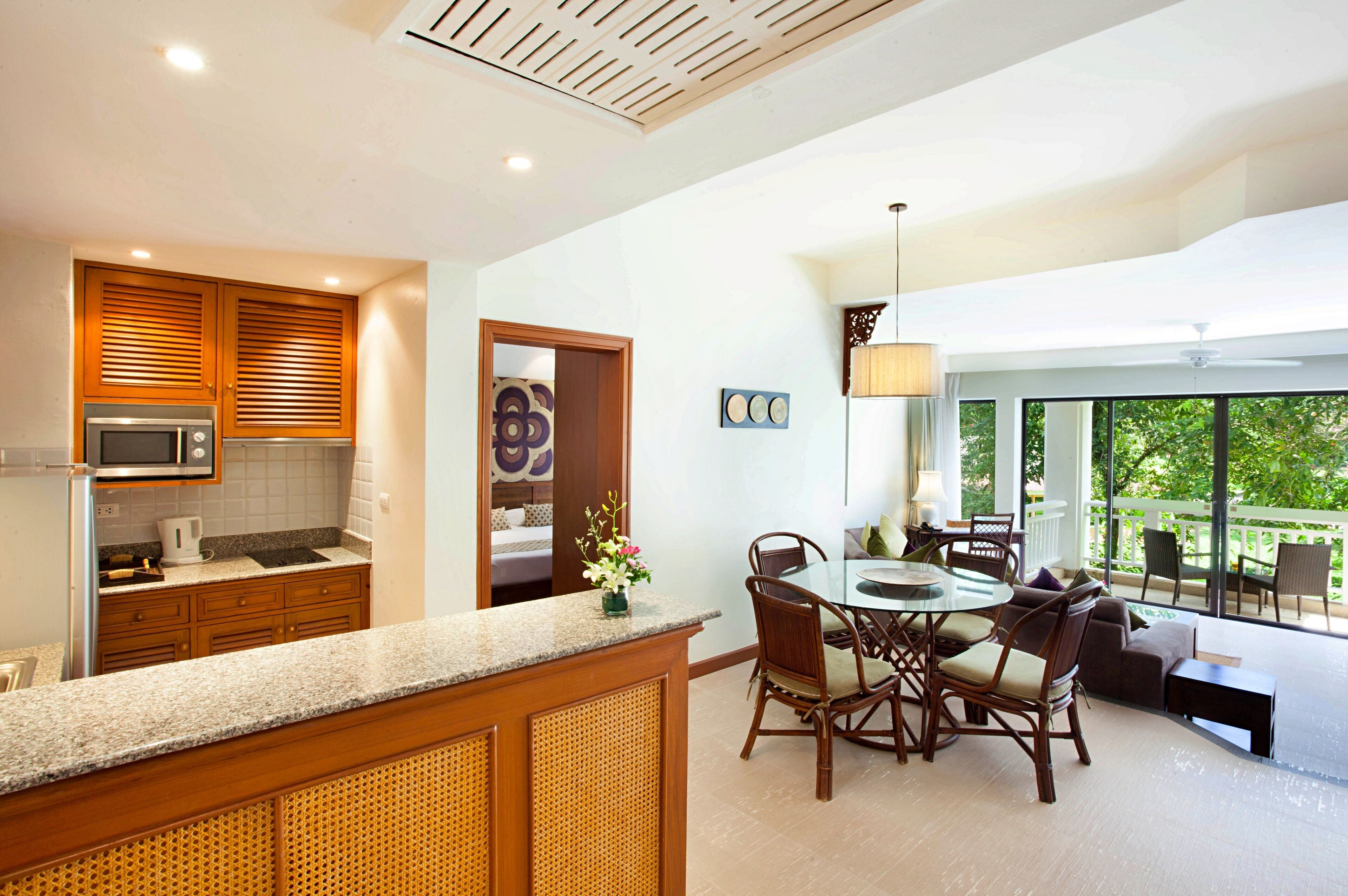 A modern kitchen with a dining area, wooden cabinets, and a view of greenery outside.