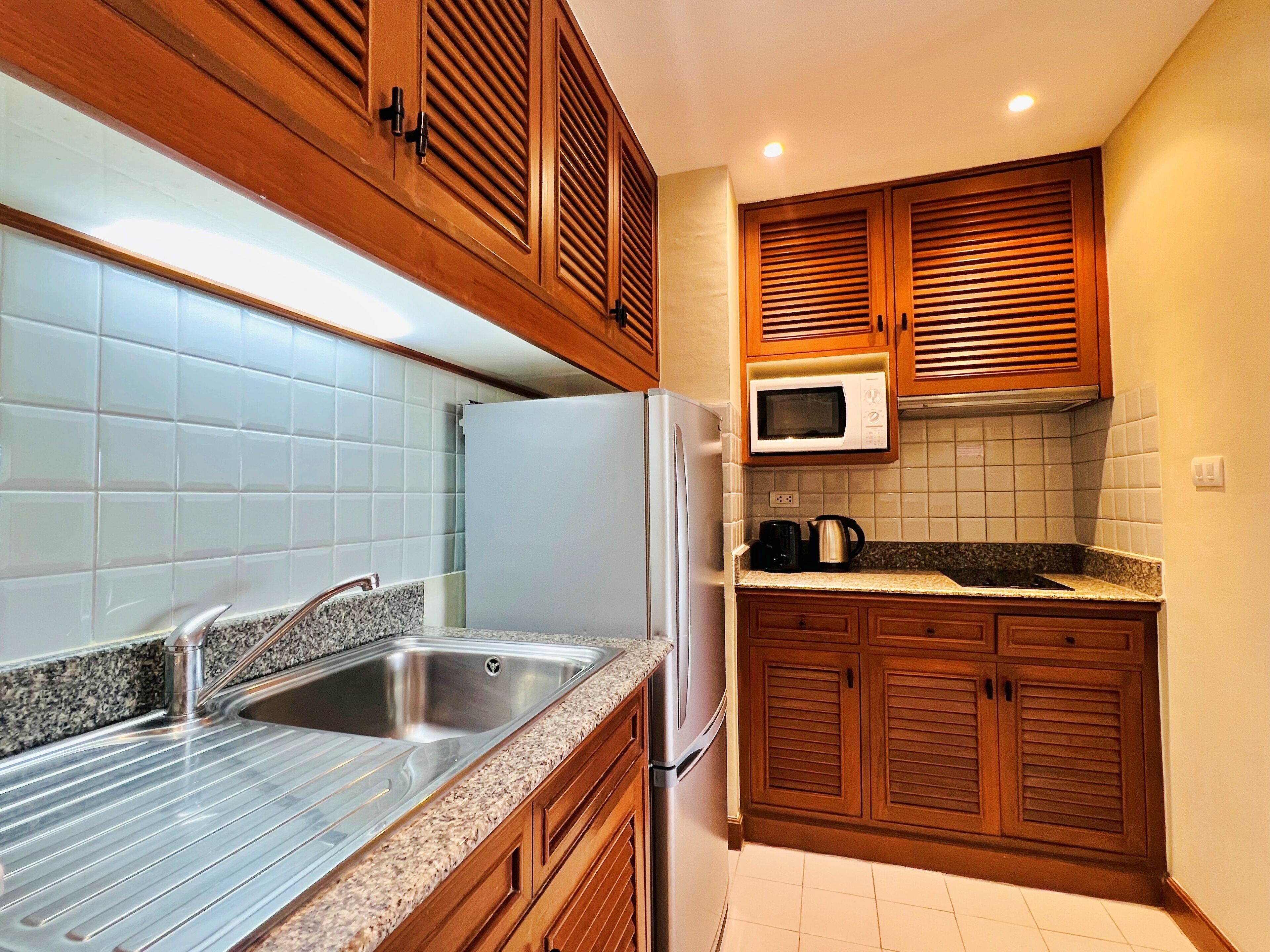 A kitchen with wooden cabinets, a stainless steel sink, a white refrigerator, and a microwave.