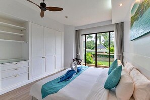A bedroom with a bed, a ceiling fan, a large window with a view of greenery, and a wardrobe. - Allamanda Laguna Phuket by RESAVA (Choeng Thale)