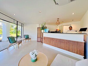 A modern reception area with a receptionist desk, seating area, and a view of the outdoors. - Allamanda Laguna Phuket by RESAVA (Choeng Thale)