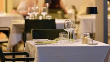 Una mesa de restaurante con mantel blanco, platos, vasos y salero y pimentero.
