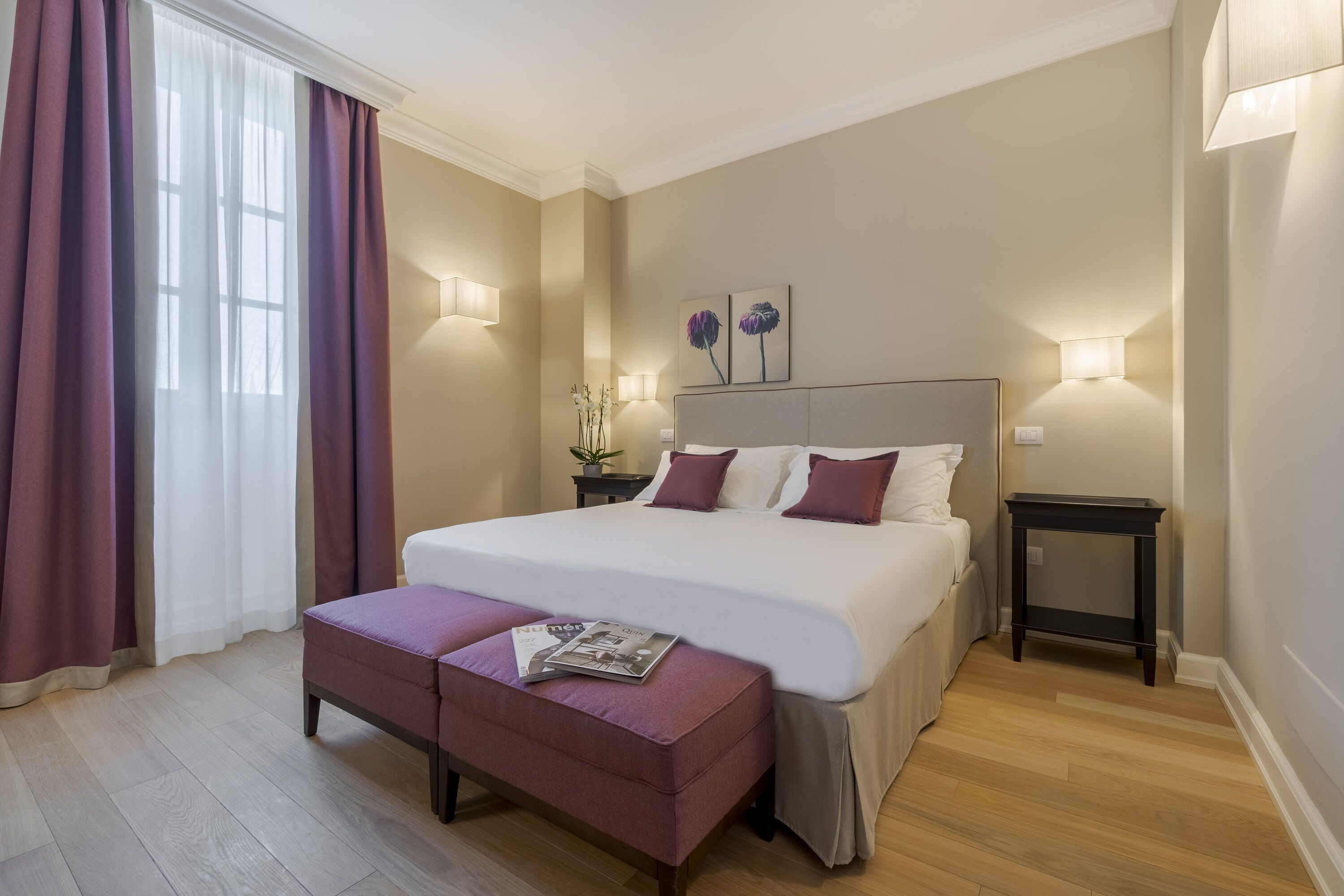 A bedroom with a large bed, a bedside table, a nightstand, and a window with curtains.