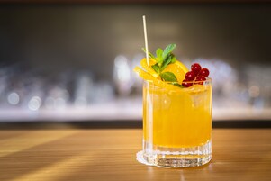A glass of orange-colored drink with garnishes on a wooden surface.