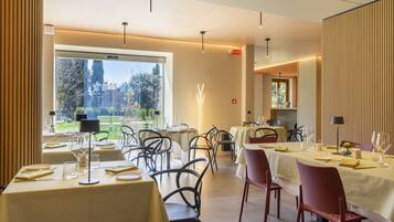 A restaurant with tables set for dining, a view of greenery outside, and a modern interior design.
