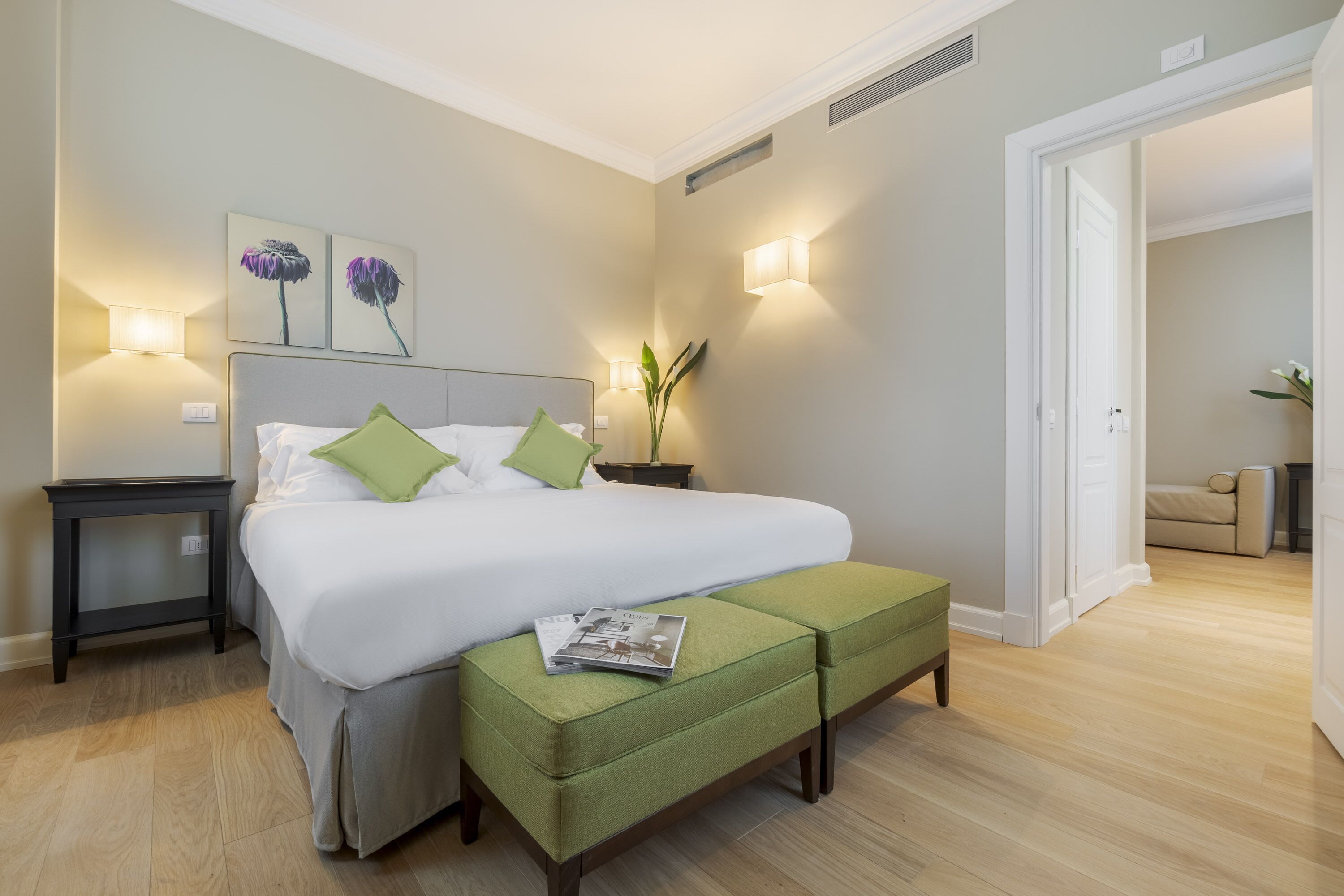 Ein ordentlich eingerichtetes Schlafzimmer mit einem großen Bett, Nachttischen, einer grünen Bank und Wandleuchten.