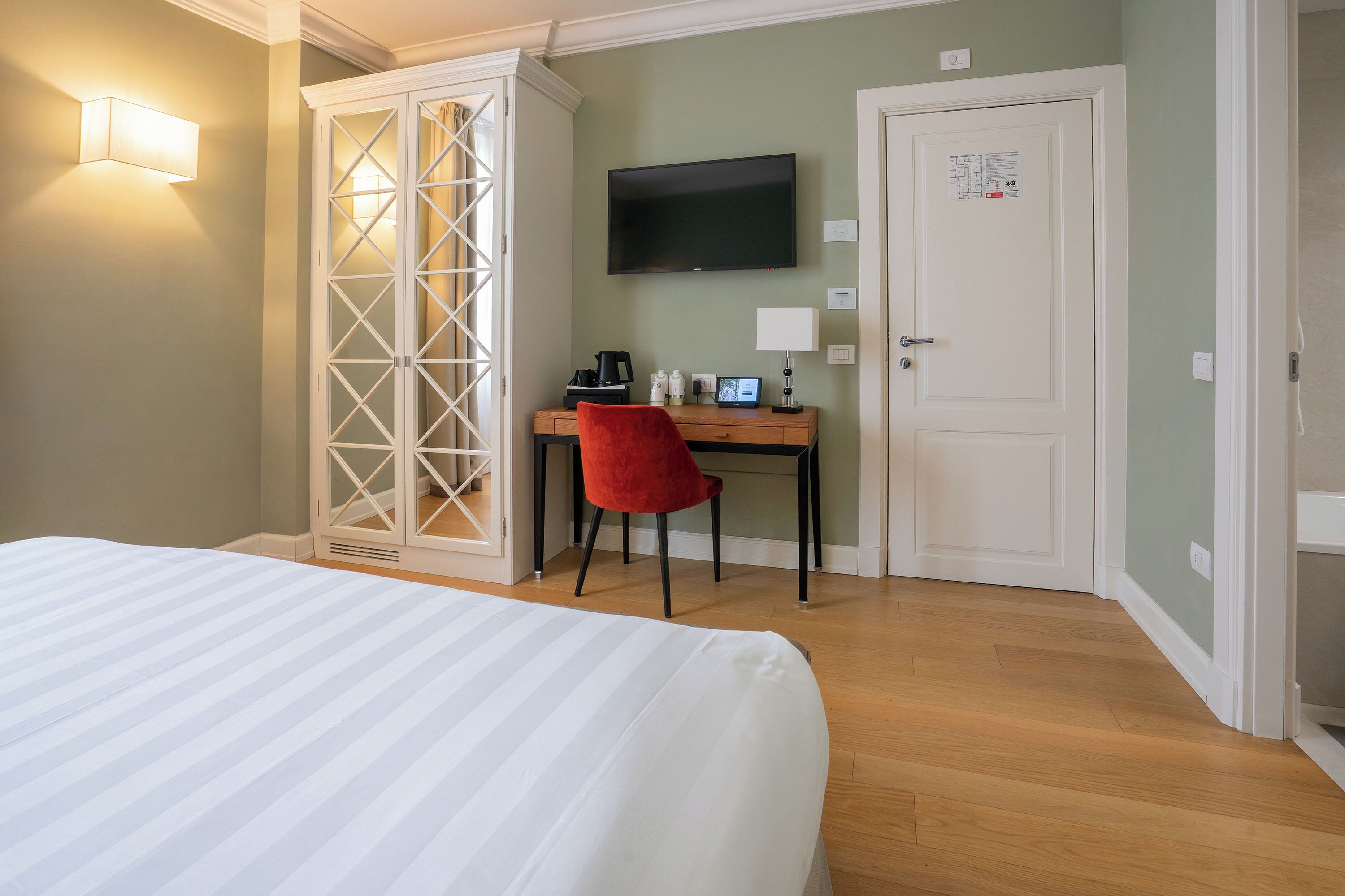 A hotel room with a bed, a desk with a chair, a television, and a wardrobe.