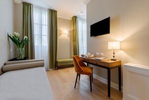 Una camera d'albergo con un letto, una scrivania con una sedia, una televisione, una lampada e un vaso con fiori.