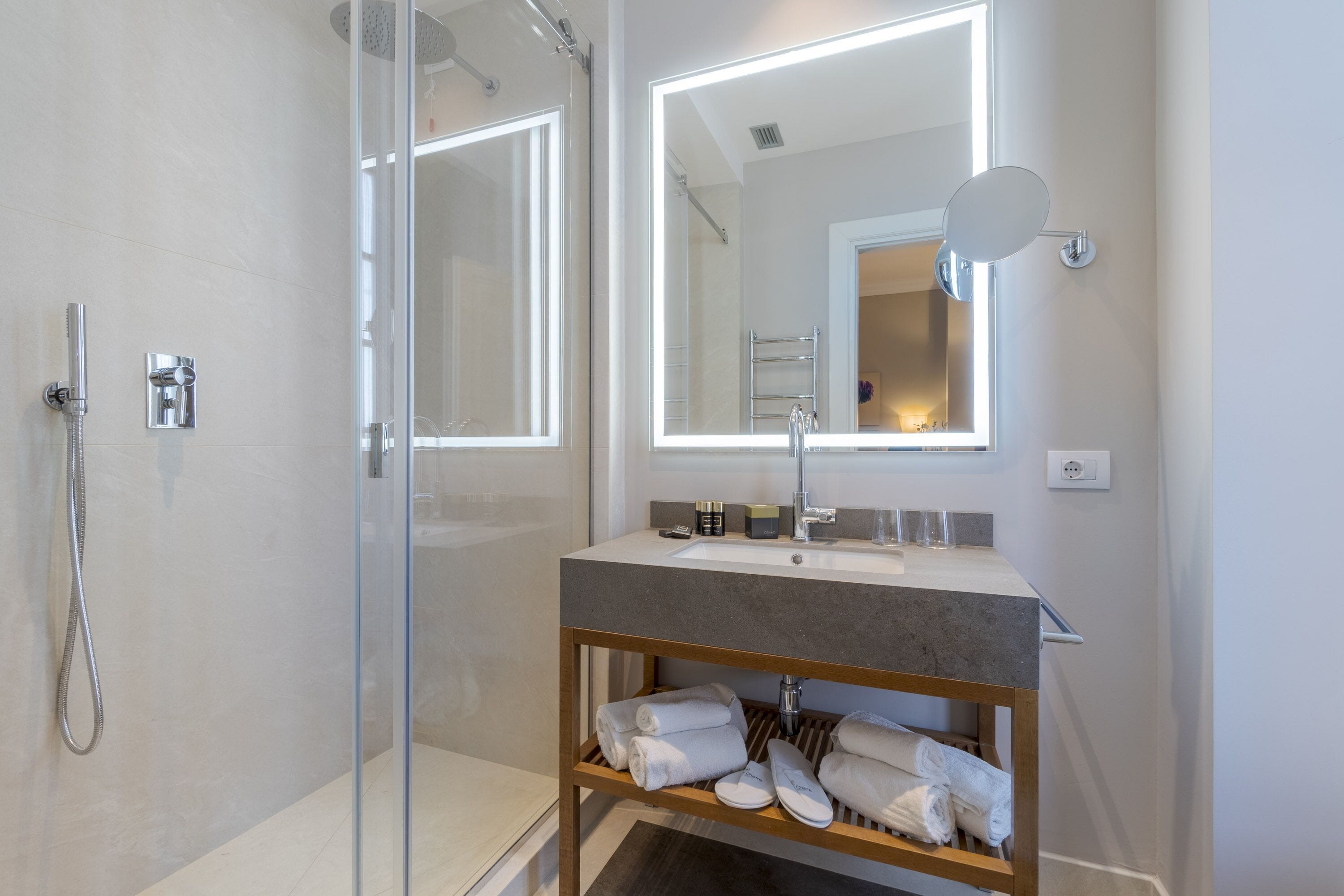 Un baño moderno con cabina de ducha de vidrio, tocador con espejo y repisa con toallas dobladas.