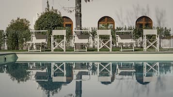 En pool med vita solstolar och en byggnad med välvda fönster.