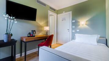 A hotel room with a bed, a desk with a chair, a TV, and a lamp.