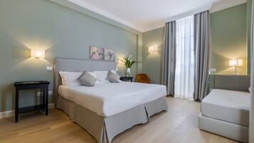 A modern hotel room with a large bed, bedside tables, a chair, and a large window with curtains.