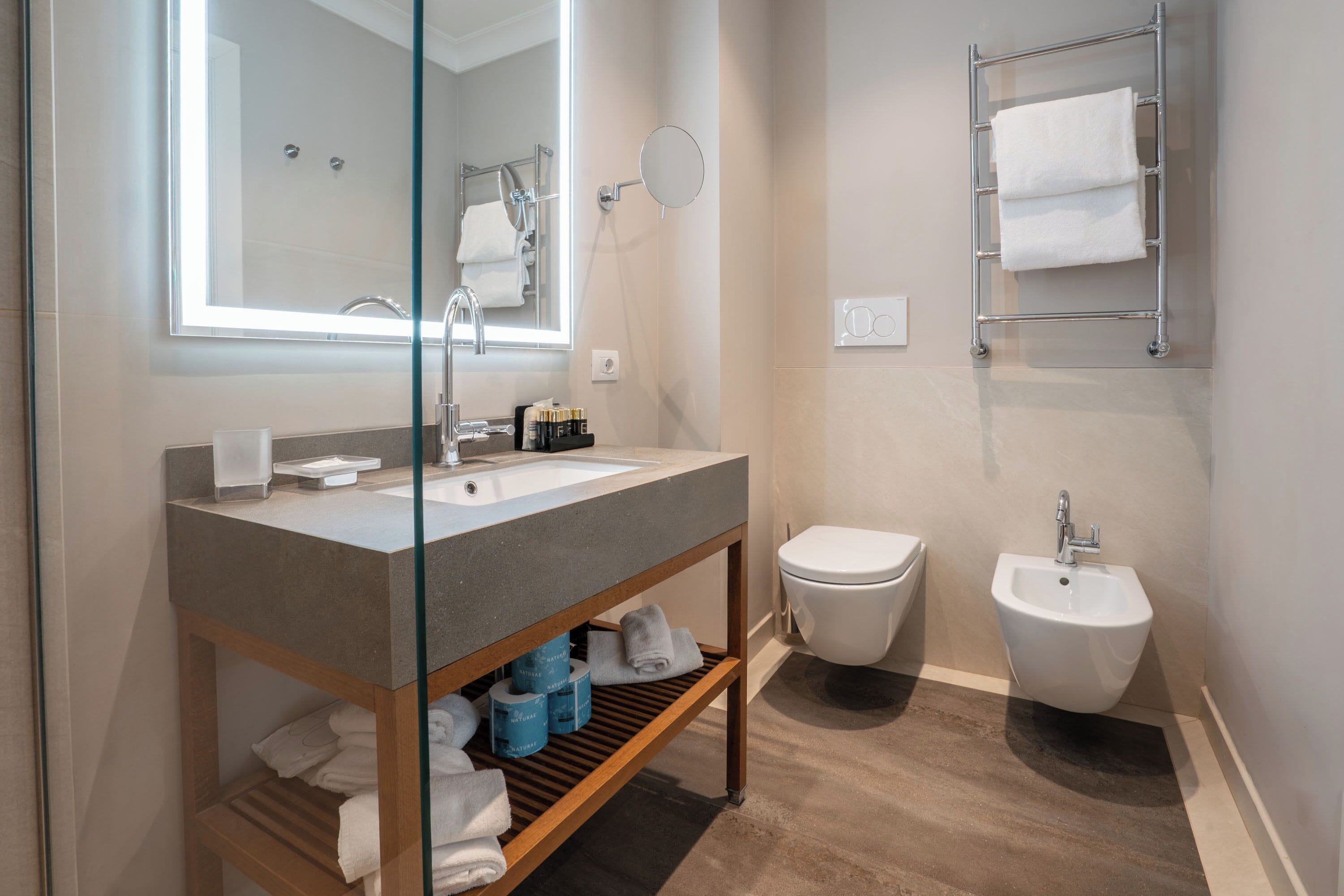 Uma casa de banho moderna com chuveiro envidraçado, toucador com lavatório, bidé e porta-toalhas.